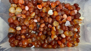 Close-up of polished 15mm heart-shaped red agate and quartz stones in a clear container