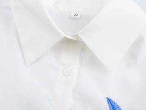 Detail of white lapel shirt collar with neat stitching and blue leaf embroidery