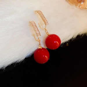 Macro shot of red faux pearl earrings with gold zircon accents on white faux fur