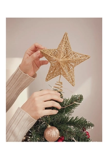 Detail of hand placing a golden glitter star topper on a Christmas tree branch