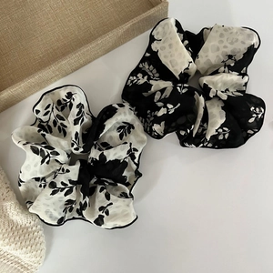 Detail of two floral bow hair scrunchies in black and white chiffon fabric on a tray