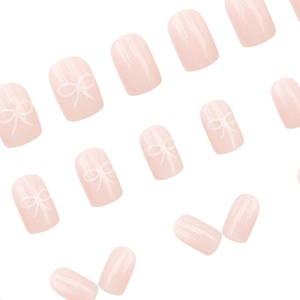 Short round nude pink press-on nails with cute white bow patterns and glossy finish