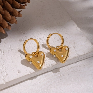 Boucles d'oreilles cœur dorées avec perles présentées sur un support en pierre