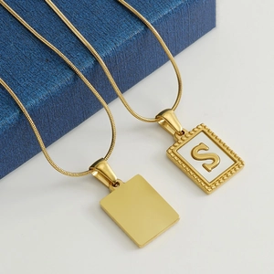 18K gold plated snake chain necklace with rectangle and letter S pendants on a blue box