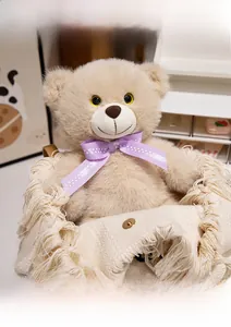 Close-up of a beige teddy bear with a purple polka dot bow in a cozy woven handbag
