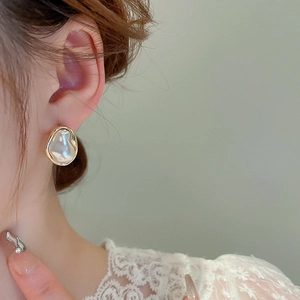 Close-up of irregular Baroque pearl earrings with gold frames on female model