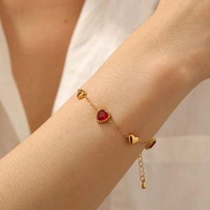Detailed view of a gold heart bracelet with red rhinestones worn on a woman's wrist
