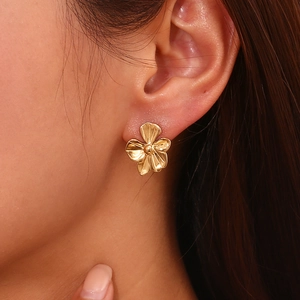 Close-up of a minimalist 18K gold plated flower stud earring worn on a female ear