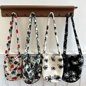 Detail view of four plush lamb wool tote bags in floral patterns hanging on wooden hooks