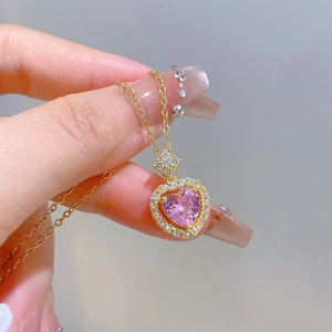 Close-up of golden necklace featuring a pink heart pendant surrounded by crystals