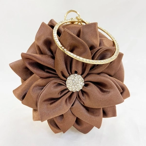 Detailed close-up of brown silk petal evening bag with rhinestone center and metal handle