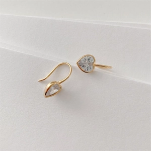 Detail view of heart-shaped gold earrings with zircon stones on white paper