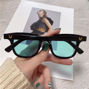 Close-up of black square sunglasses with mint green lenses and metal V-shaped logo detail