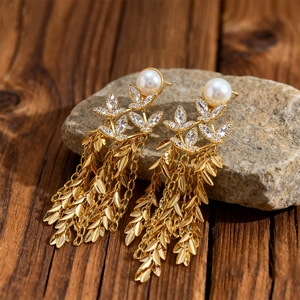 Detailed close-up of 18K gold-plated leaf tassel earrings with white pearls and crystals