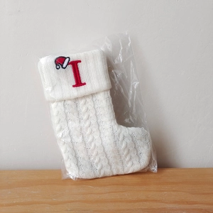 Close-up of a white knitted Christmas stocking with a red embroidered letter I and Santa hat
