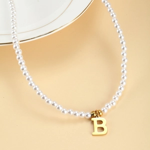 Elegant gold letter B pendant with white pearl necklace on minimalist beige background