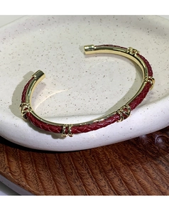 Dettaglio ravvicinato di un bracciale in pelle intrecciata rossa con accenti dorati su vassoio