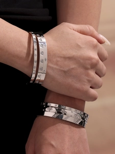 Close-up of stacked silver stainless steel bracelets with geometric patterns and zircons