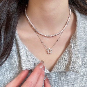 Close-up of double-layered necklace with pearls and flower pendant on silver chain
