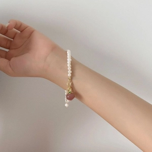 Detailed shot of fresh water pearl bracelet featuring golden clasp and pink heart charm