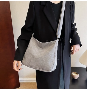 Detail view of large grey corduroy crossbody bag worn with a stylish black blazer