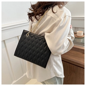 Detail of black quilted tote bag with gold chain strap worn by a model in interior setting