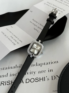 Close-up of a silver square watch with diamond bezel and black leather strap on a magazine