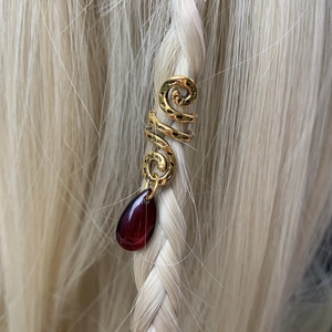 Detailed close-up of golden spiral hair bead with a deep red teardrop crystal on blonde braid