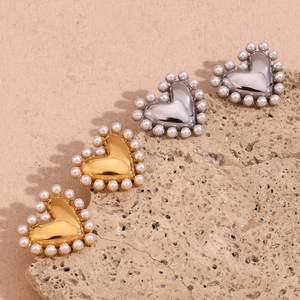 Close-up of gold and silver heart earrings with pearl trim on a textured stone base