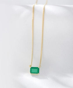 Detailed close-up of emerald-cut green gemstone on a delicate gold chain necklace