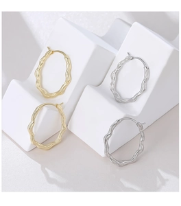 Macro shot of silver and gold wave-textured hoop earrings on a minimalist white platform