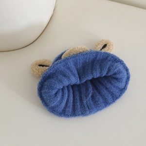 Close-up of royal blue knitted hat with soft beige plush bear ears on white leather