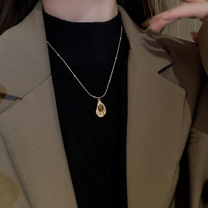 Close-up of a gold vintage necklace with a brown tiger eye stone pendant on a model