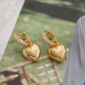 Detail of 3D gold heart earrings with micro-pave cubic zirconia on a textured green background
