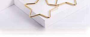Detail polierter goldener Ohrringe in Sternform auf weißem Holzhintergrund