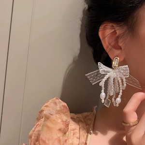 Close-up of elegant bow earrings with pearl tassels and crystals on a model