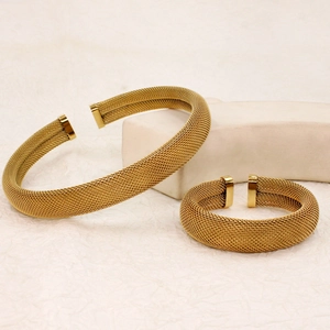 Detail of two gold mesh woven open bracelets on a minimalist textured background