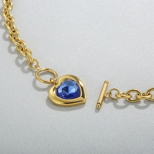 Détail macro du collier chaîne dorée avec pendentif cœur en cristal bleu et fermoir à bascule