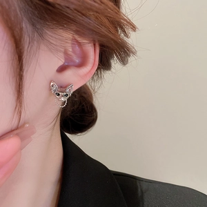 Detail of silver cat earring with black eyes and chain on model's ear