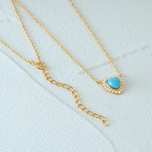 Detail of gold heart pendant featuring a blue gemstone and pavé stones on a fine chain