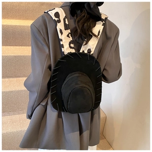 Detail view of a black suede cowboy hat-shaped backpack with cow-print shoulder straps