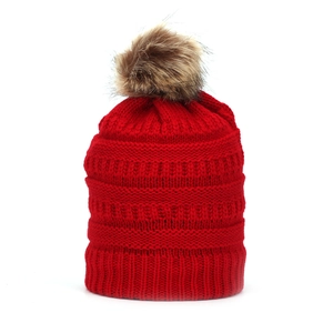 Close-up of red winter knit beanie featuring thick vertical ribs and a faux fur pompom