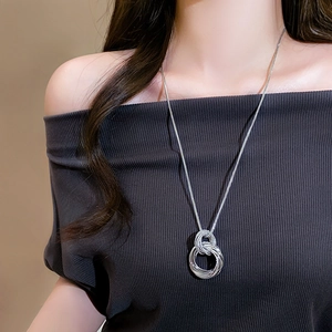 Collier minimaliste argenté avec pendentif à anneaux torsadés sur un pull en maille foncé