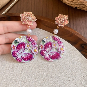 Detail of pink floral acrylic earrings with gold rose motifs and pearl accents