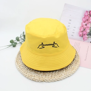 Bright yellow cotton bucket hat with black 'something' embroidery on woven mat