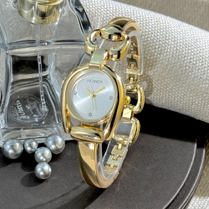 Detail of a golden horseshoe bangle watch with silver dial and horsebit chain strap