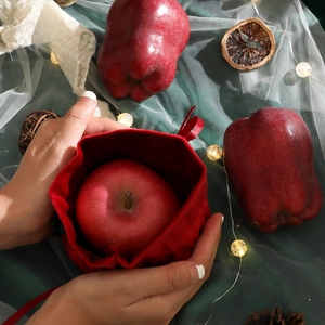 Festive red velvet drawstring Christmas apple gift bag with satin ribbon on holiday background