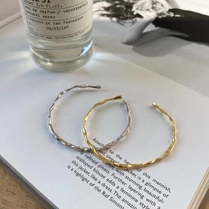 Irregular wave open bangles in gold and silver finish on a lifestyle magazine background