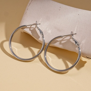 Polished silver geometric hoop earrings displayed on a minimalist stone pedestal