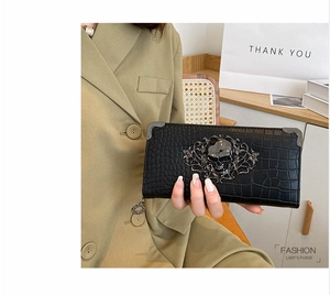 Detail of black crocodile texture clutch with vintage silver skull emblem and metal corners